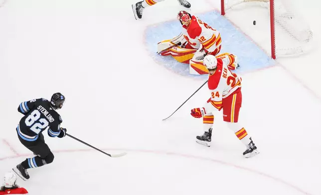 Utah Hockey Club center Kevin Stenlund (82) shoots and scores a goal past Calgary Flames goaltender Dustin Wolf (32) during the first period of an NHL hockey game, Tuesday, April 1, 2025, in Salt Lake City. (AP Photo/Tyler Tate)
