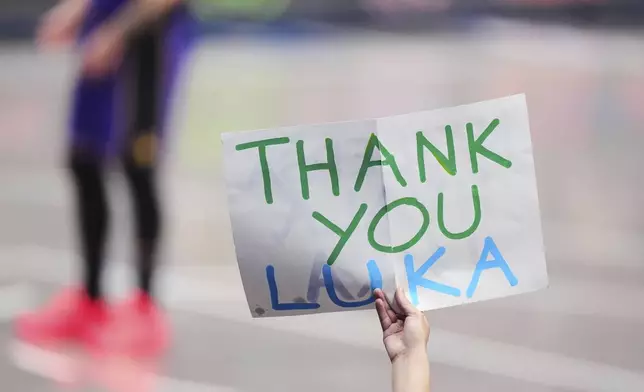 A fan holds up a sign thanking Los Angeles Lakers' Luka Doncic as he stands on the court at rear late in the second half of an NBA basketball game against the Dallas Mavericks in Dallas, Wednesday, April 9, 2025. (AP Photo/LM Otero)