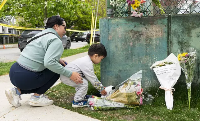 A young child and his mother leave a teddy bear and flowers, near the location where a vehicle drove into crowd at a street festival, in Vancouver, Sunday April 27, 2025. (Rich Lam/The Canadian Press via AP)