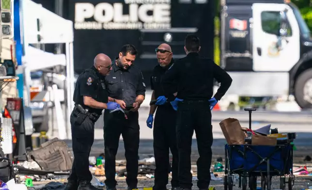 Members of the Vancouver Police forensics team examine a victim's phone while investigating the scene where a vehicle drove into a crowd Saturday killing multiple people at a street festival, in Vancouver, British Columbia, Sunday, April 27, 2025. (Rich Lam/The Canadian Press via AP)