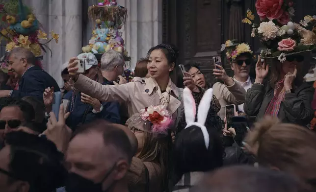 An attendee takes a selfie wearing decorated hats and costumes during the annual Easter Parade and Bonnet Festival in front of St. Patrick's Cathedral on Sunday, April 20, 2025, in New York. (AP Photo/Andres Kudacki)