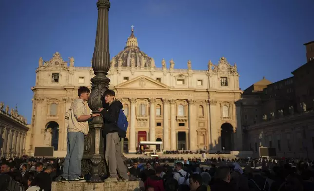 Faithful stand in a lamppost as they wait for the funeral of Pope Francis to begin in St. Peter's Square, at the Vatican, Saturday, April 26, 2025. (AP Photo/Emilio Morenatti)