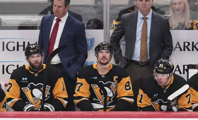 Pittsburgh Penguins' Bryan Rust (17), Sidney Crosby (87), and Evgeni Malkin (71) sit on the bench in front of head coach Mike Sullivan, left rear, and assistant coach Mike Vellucci during the third period of an NHL hockey game against the Boston Bruins in Pittsburgh, Sunday, April 13, 2025. (AP Photo/Gene J. Puskar)