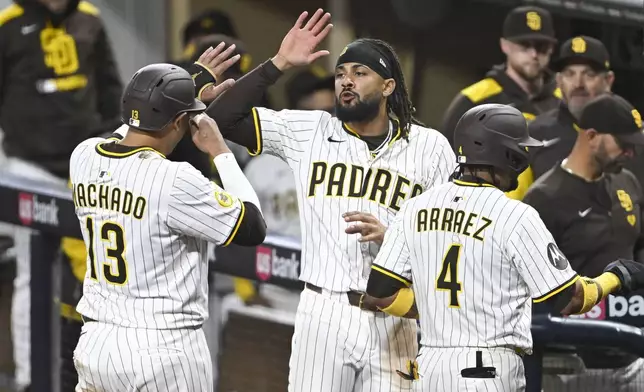 San Diego Padres right fielder Fernando Tatis Jr. (23), center, and Manny Machado (13), left, high-five after two-runs scored during the seventh inning of a baseball game against the Chicago Cubs Monday, April 14, 2025, in San Diego, Calif. (AP Photo/Denis Poroy)