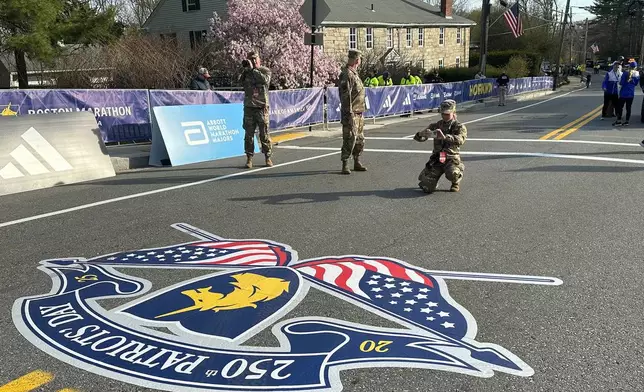Massachusetts Army National Guard Cadet Meghan Drysdale kneels to take a photo of the road painted in commemoration of the 250th anniversary of Patriots' Day at the start of the Boston Marathon Monday, April 21, 2025. (AP Photo Jennifer McDermott)