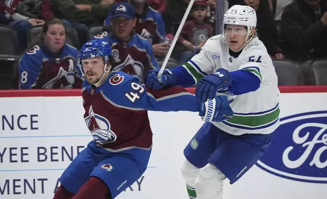 Colorado Avalanche defenseman Samuel Girard, left, checks Vancouver Canucks center Aatu Raty, right, as they pursue the puck in the second period of an NHL hockey game Thursday, April 10, 2025, in Denver. (AP Photo/David Zalubowski)