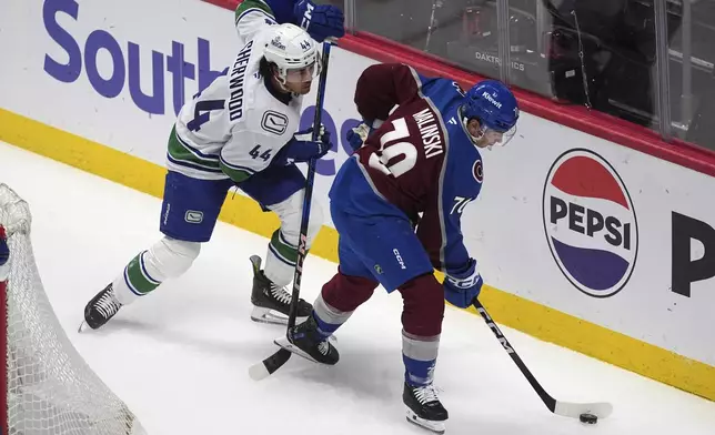 Colorado Avalanche defenseman Sam Malinski, right, collects the puck as Vancouver Canucks left wing Kiefer Sherwood, left, defends in the first period of an NHL hockey game Thursday, April 10, 2025, in Denver. (AP Photo/David Zalubowski)