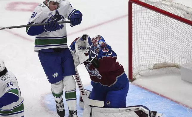Colorado Avalanche goaltender Mackenzie Blackwood, right, makes a glove-save of a shot while screened by the Vancouver Canucks center Linus Karlsson (94) in the first period of an NHL hockey game Thursday, April 10, 2025, in Denver. (AP Photo/David Zalubowski)