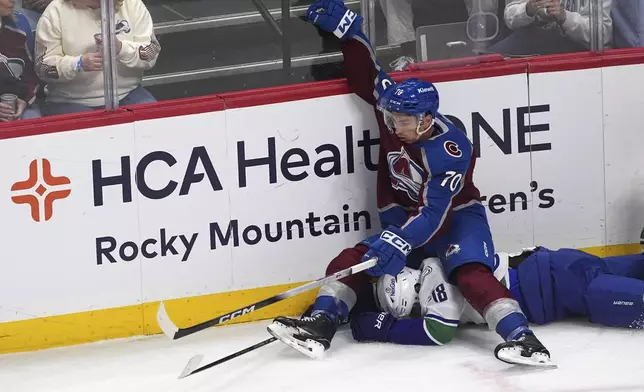 Colorado Avalanche defenseman Sam Malinski, top, lands on Vancouver Canucks left wing Drew O'Connor as they pursue the puck in the first period of an NHL hockey game Thursday, April 10, 2025, in Denver. (AP Photo/David Zalubowski)
