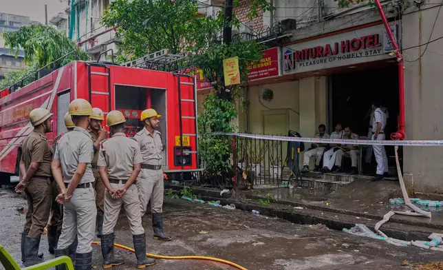 Firefighters stand as policemen guard the entrance of a hotel building which caught fire on Tuesday resulting in several deaths, in Kolkata, India, Wednesday, April 30, 2025. (AP Photo/Bikas Das)