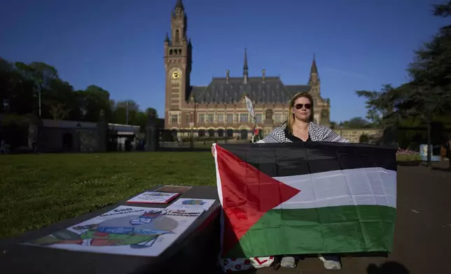 A protestor with a Palestinian flag waits for others to arrive at the International Court of Justice which opens hearings into a United Nations request for an advisory opinion on Israel's obligations to allow humanitarian assistance in Gaza and the West Bank, in The Hague, Netherlands, Monday, April 28, 2025. (AP Photo/Peter Dejong)