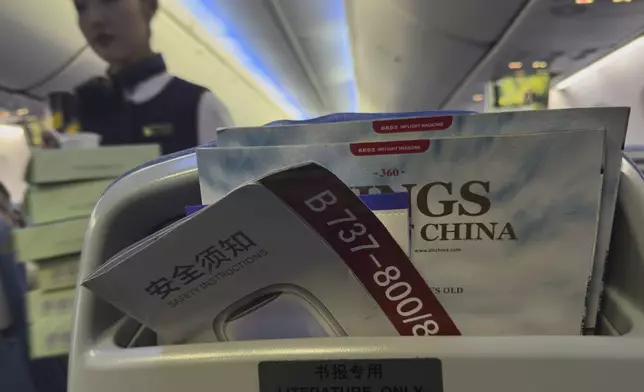 A stewardess walks by a seat compartment displaying a safety instruction leaflet of an Air China airlines Boeing 737-800 together with magazines on a seat compartment during a flight in China, Wednesday, April 16, 2025. (AP Photo/Andy Wong)