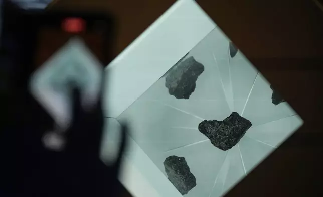 A visitor takes a photo of rocks of the moon displayed at the U.S. pavilion on the opening day of the Expo 2025 in Osaka, central Japan, Sunday, April 13, 2025. (AP Photo/Hiro Komae)