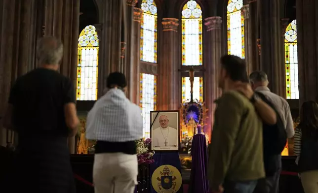 People stand next to a photograph of Pope Francis placed at Saint Anthony Catholic church in Istanbul, Turkey, Monday, April 21, 2025. (AP Photo/Khalil Hamra)