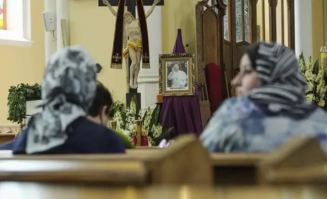 Parishioners sit around a photo of the late Pope Francis after the news of his death at age 88 at the Cathedral of the Immaculate Conception in Moscow, Russia, Monday, April 21, 2025. (AP Photo/Pavel Bednyakov)