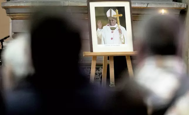 Believers sit in front of a photo of the late Pope Francis after the news of his death, during a Easter service at the Basilica of St. John the Baptist, near the Vatican embassy, in Berlin, Germany, Monday, April 21, 2025. (AP Photo/Markus Schreiber)