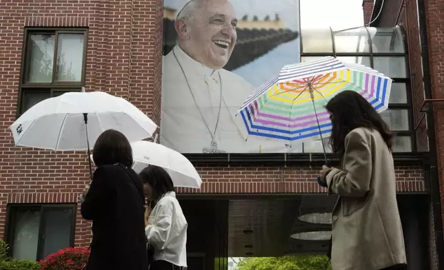 People pass by a portrait of Pope Francis at Myeongdong Cathedral in Seoul, South Korea, Tuesday April 22, 2025. (AP Photo/Ahn Young-joon)