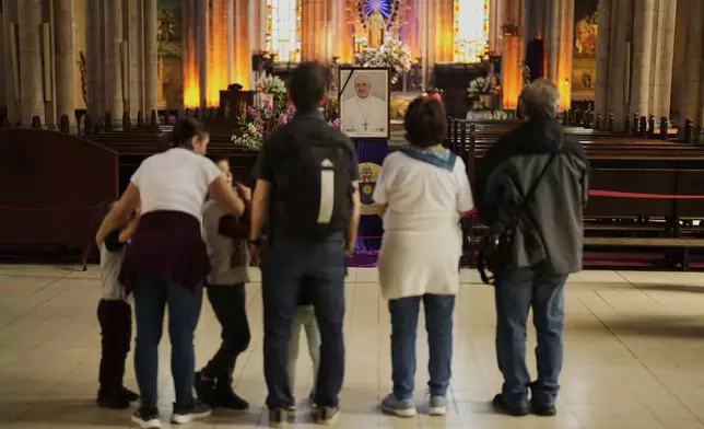 People stand next to a photograph of Pope Francis placed at Saint Anthony Catholic church in Istanbul, Turkey, Monday, April 21, 2025. (AP Photo/Khalil Hamra)