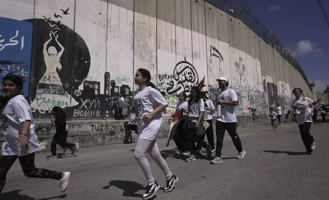 Youth take part in the "Run the Wall" activity to raise awareness on the ongoing situation in the Gaza Strip and in the West Bank, as they run past the Israel's separation barrier in the West Bank city of Bethlehem, Friday, April 25, 2025. (AP Photo/Mahmoud Illean)