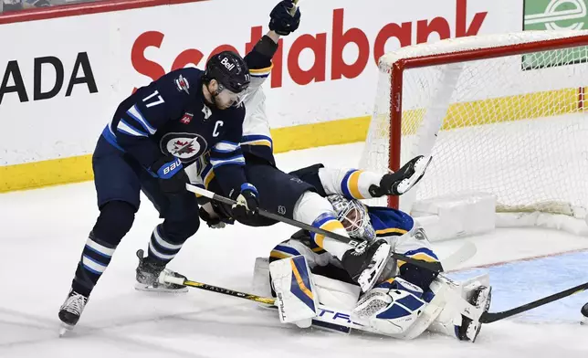 St. Louis Blues' Jake Neighbours, center, falls over Blues goaltender Jordan Binnington, right, as he is checked by Winnipeg Jets' Adam Lowry (17) during the third period of Game 2 of a first-round NHL hockey playoff series in Winnipeg, Manitoba, Monday April 21, 2025. (Fred Greenslade/The Canadian Press via AP)