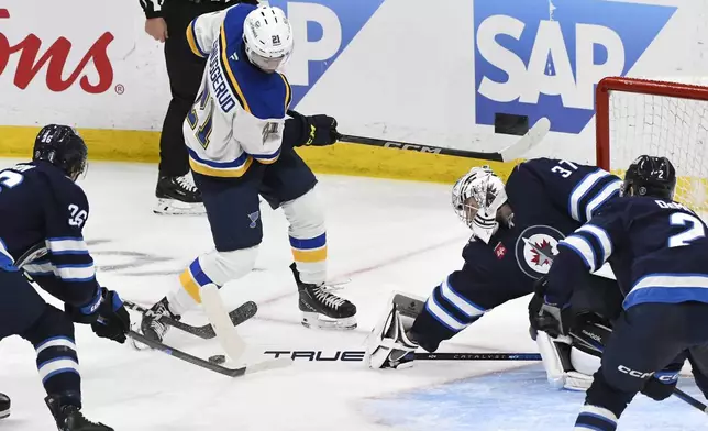 Winnipeg Jets goaltender Connor Hellebuyck (37) makes a save against St. Louis Blues' Jimmy Snuggerud (21) during the third period of Game 2 of a first-round NHL hockey playoff series in Winnipeg, Manitoba, Monday April 21, 2025. (Fred Greenslade/The Canadian Press via AP)