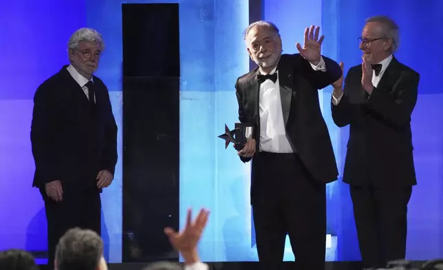 Francis Ford Coppola, second from right, waves to the audience as presenters George Lucas, left, and Steven Spielberg look on during the 50th AFI Life Achievement Award tribute to Coppola on Saturday, April 26, 2025, at the Dolby Theatre in Los Angeles. (AP Photo/Chris Pizzello)