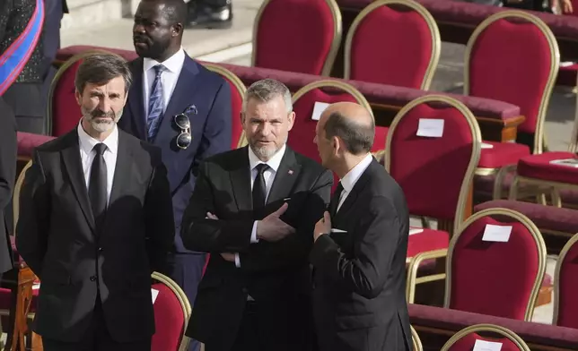 Slovakia's President Peter Pellegrini, center, and Slovakia's Foreign Minister Juraj Blanar, left, stand in front of their seats ahead of the funeral of Pope Francis in St. Peter's Square at the Vatican, Saturday, April 26, 2025. (AP Photo/Markus Schreiber)