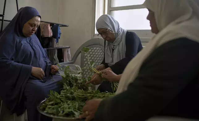 Salha Farhat, 68, center, separates herbs for a meal as she sits with two Palestinian women at a youth center that has been used as a temporary shelter for displaced people in the West Bank city of Tulkarem, Thursday, April 3, 2025. (AP Photo/Leo Correa)