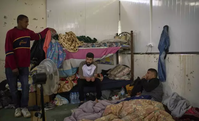 Palestinian men talk as they stand in compound of a local multipurpose hall, that is been used as a temporary shelter for displaced people in the village of Kafr al-Labad, near the West Bank city of Tulkarem, Thursday, April 3, 2025. (AP Photo/Leo Correa)