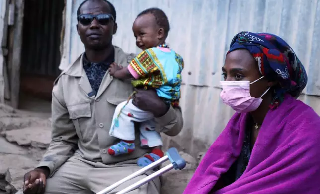 Chandera Weldesenbet, 41-year-old, left, a wounded former combatant of the recent war, sits outside his home carrying his one-and-a-half-year-old child and his wife Rahel Gebrekidan, right, in Quiha, Tigray region of northern Ethiopia Friday, Feb. 14, 2025. (AP Photo/Amanuel Birhane)