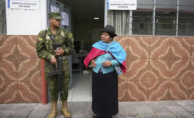 A voter stands next to a soldier guarding a polling station during the presidential election runoff in Quito, Ecuador, Sunday, April 13, 2025. (AP Photo/Carlos Noriega)