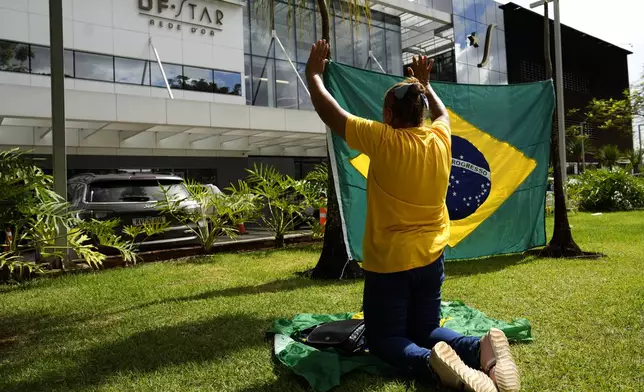 A supporter of former President Jair Bolsonaro prays outside DF Star hospital where he had abdominal surgery in Brasilia, Brazil, Monday, April 14, 2025. (AP Photo/Eraldo Peres)