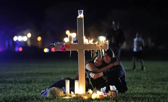 FILE - People comfort each other as they sit and mourn at one of seventeen crosses, Feb. 15, 2018, after a candlelight vigil for the victims of the shooting at Marjory Stoneman Douglas High School, in Parkland, Fla. (AP Photo/Gerald Herbert, File)