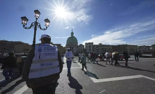 Stewards check tourists' QR codes outside the main train station in Venice, Italy, Friday, April 18, 2025, as the city for a second year is charging day-trippers an arrivals tax. (AP Photo/Antonio Calanni)
