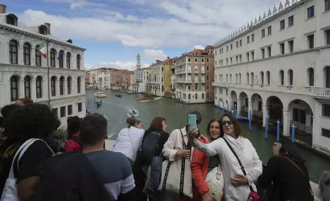Tourists take pictures on Rialto Bridge "Ponte di Rialto" in Venice, Italy, Friday, April 18, 2025, Venice on Friday launches for a second year a pilot program to charge day-trippers an entrance fee. (AP Photo/Antonio Calanni)