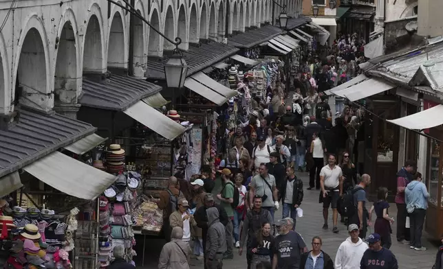 Tourists walk in Venice, Italy, Friday, April 18, 2025, Venice on Friday launches for a second year a pilot program to charge day-trippers an entrance fee. (AP Photo/Antonio Calanni)