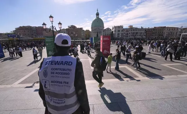 Stewards check tourists' QR codes outside the main train station in Venice, Italy, Friday, April 18, 2025, as the city for a second year is charging day-trippers an arrivals tax. (AP Photo/Antonio Calanni)