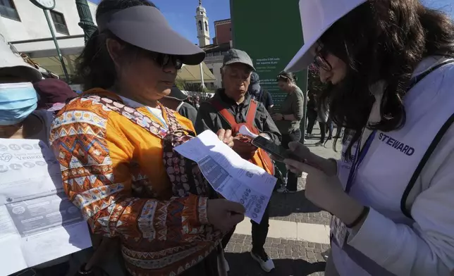 Stewards check tourists' QR codes outside the main train station in Venice, Italy, Friday, April 18, 2025, as the city for a second year is charging day-trippers an arrivals tax. (AP Photo/Antonio Calanni)