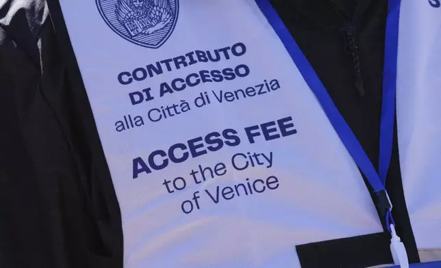 A steward's gilet states an arrival tax fee for tourists visiting Venice, Italy, Friday, April 18, 2025. (AP Photo/Antonio Calanni)