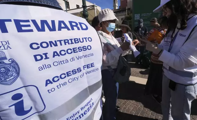 Stewards check tourists' QR codes outside the main train station in Venice, Italy, Friday, April 18, 2025, as the city for a second year is charging day-trippers an arrivals tax. (AP Photo/Antonio Calanni)