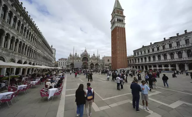 People walk in San Marco square in Venice, Italy, Friday, April 18, 2025, Venice on Friday launches for a second year a pilot program to charge day-trippers an entrance fee. (AP Photo/Antonio Calanni)
