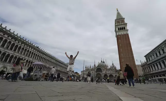 A tourist jumps in San Marco square in Venice, Italy, Friday, April 18, 2025, Venice on Friday launches for a second year a pilot program to charge day-trippers an entrance fee. (AP Photo/Antonio Calanni)