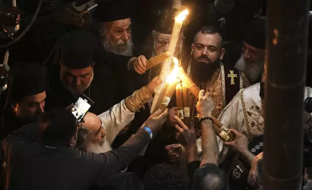 Greek Orthodox Patriarch of Jerusalem Theophilos III, left, light candles for Christian pilgrims during the Holy Fire ceremony, at the Church of the Holy Sepulcher, the site where according to tradition Jesus was crucified and buried, in Jerusalem's Old City, Saturday, April 19, 2025. (AP Photo/Mahmoud Illean)