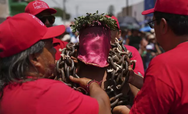 A masked penitent is helped with the chains he bears during a Holy Week procession in Atlixco, Mexico, on Good Friday, April 18, 2025. (AP Photo/Eduardo Verdugo)