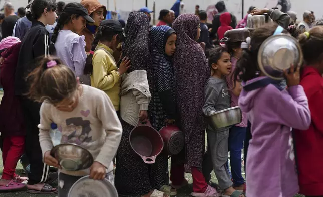 Palestinians wait for donated food at a distribution center in Nuseirat, central Gaza Strip, Friday, April 11, 2025. (AP Photo/Abdel Kareem Hana)