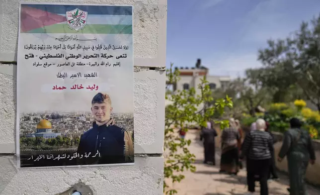 Palestinian women walk past a poster showing Waleed Ahmad that reads in Arabic, "The hero prisoner Martyr, mercy and eternity for our righteous Martyrs," in the West Bank town of Silwad, northeast of Ramallah, Wednesday, March 26, 2025. (AP Photo/Nasser Nasser)