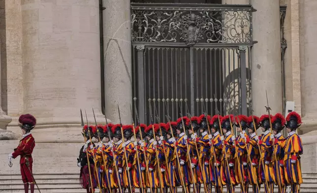 Pontifical Swiss guards stand in formation in St. Peter's Square as people await the arrival of the body of Pope Francis, who will lie in state at St. Peter's Basilica for three days, at the Vatican, Wednesday, April 23, 2025. (AP Photo/Bernat Armangue)