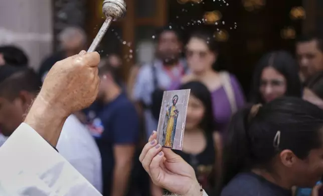 A priest sprinkles "holy water" on a St. Mark religious card during St. Mark’s Fair, a month-long event honoring the saint, outside St. Mark's Church in Aguascalientes, Mexico, Friday, April 25, 2025. (AP Photo/Eduardo Verdugo)