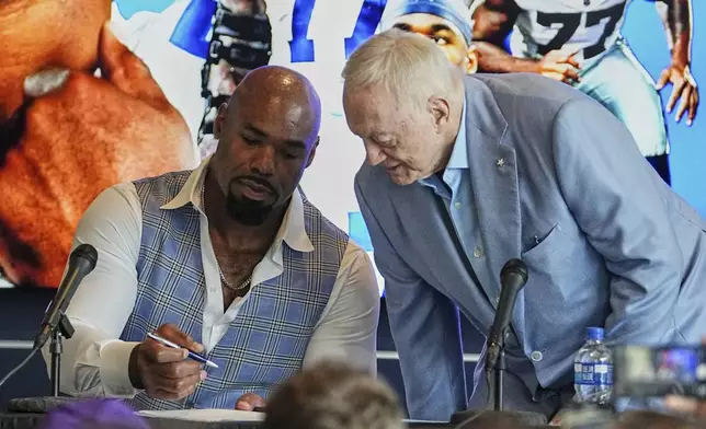 Football player Tyron Smith, left, signs a contract as Dallas Cowboys team owner Jerry jones, right, takes a seat during a news conference where Smith announced his retirement from the NFL at the Cowboys headquarters in Frisco, Texas, Wednesday, April 16, 2025. (AP Photo/Tony Gutierrez)