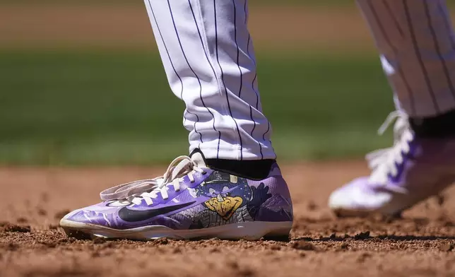 Colorado Rockies' Zac Veen wears a pair of cleats with the image of the team's mascot, Dinger the dinosaur, as he leads off first base in the third inning of a baseball game against the Milwaukee Brewers Thursday, April 10, 2025, in Denver. (AP Photo/David Zalubowski)
